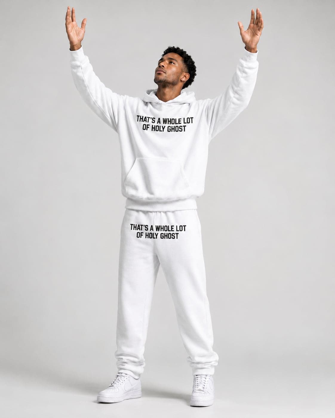 Man in a white That's A Whole Lot Of Holy Ghost sweatsuit lifting his hands in praise
