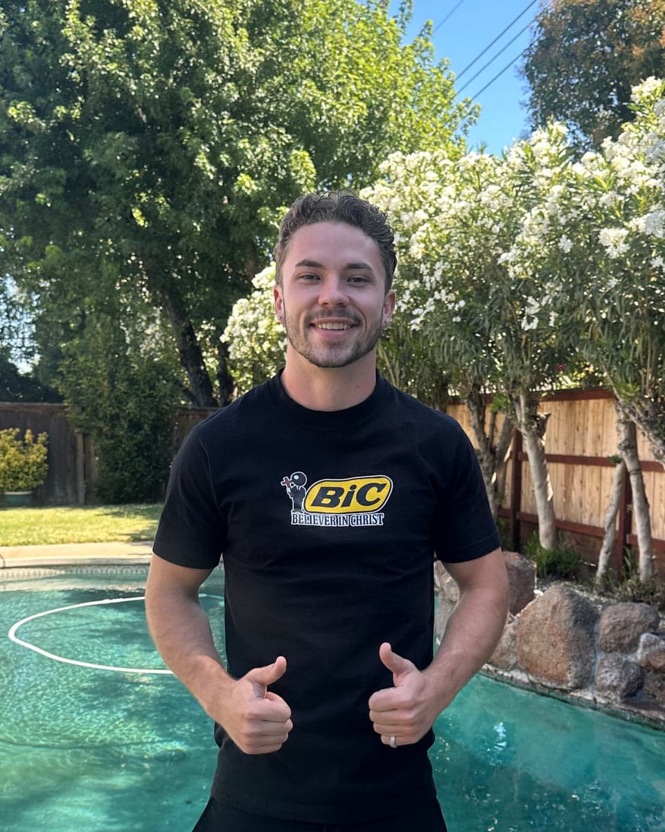 Jaron Fox in a black Believer In Christ tee, giving two thumbs up beside a pool